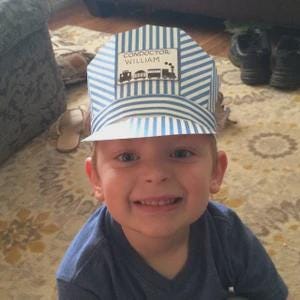 Child wearing a blue striped conductor's cap for dramatic play centers