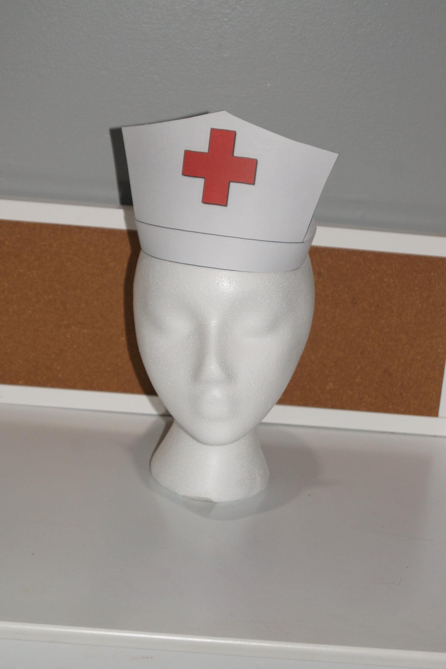 White printable nurse hat with red cross displayed on a mannequin head for community helper and dramatic play activities
