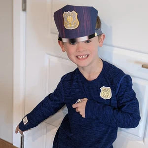 Child wearing a police costume with a hat and badge, standing indoors.